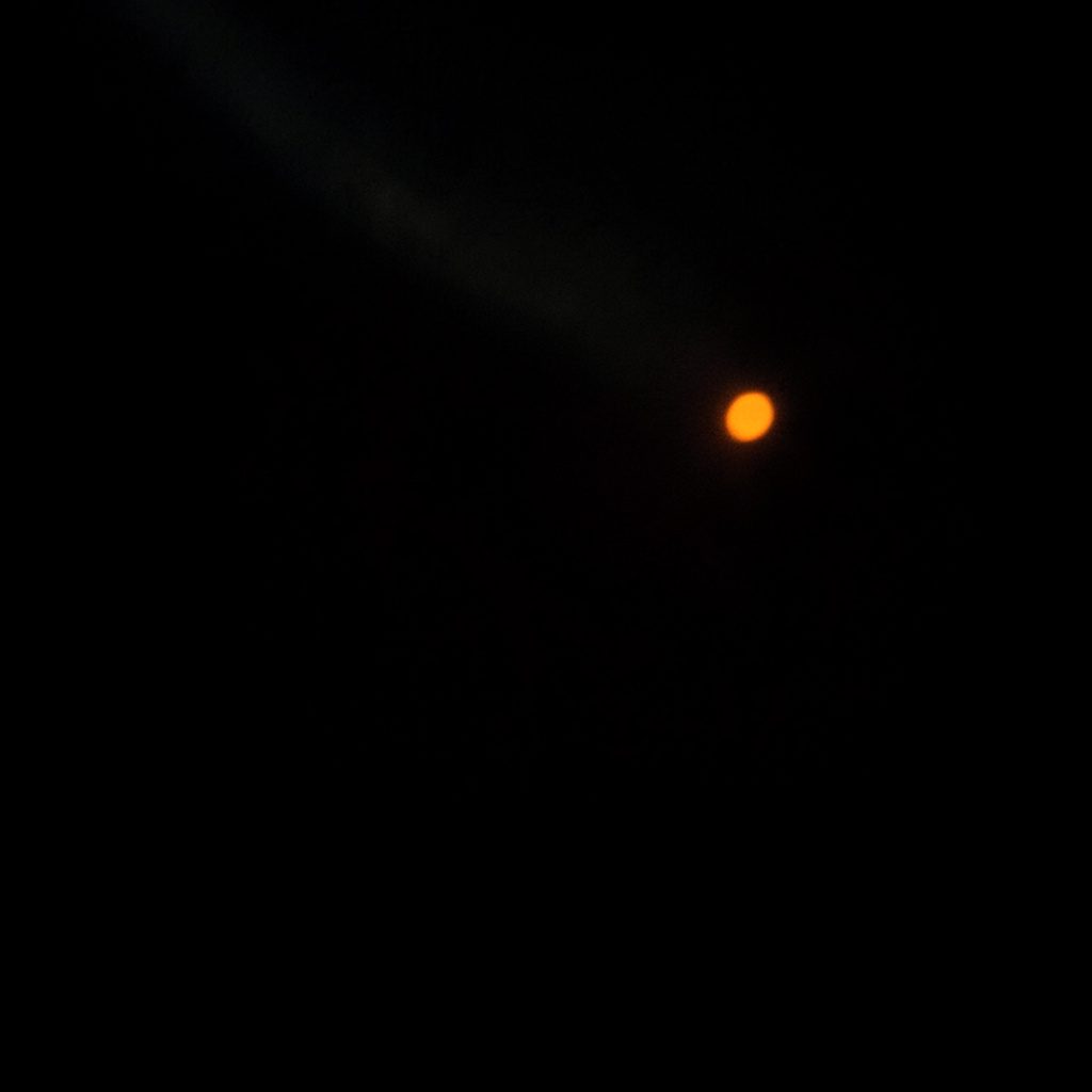 Dark, low-key photograph of a shield icon glowing on a computer screen in a dim room, suggesting cybersecurity and threat protection.